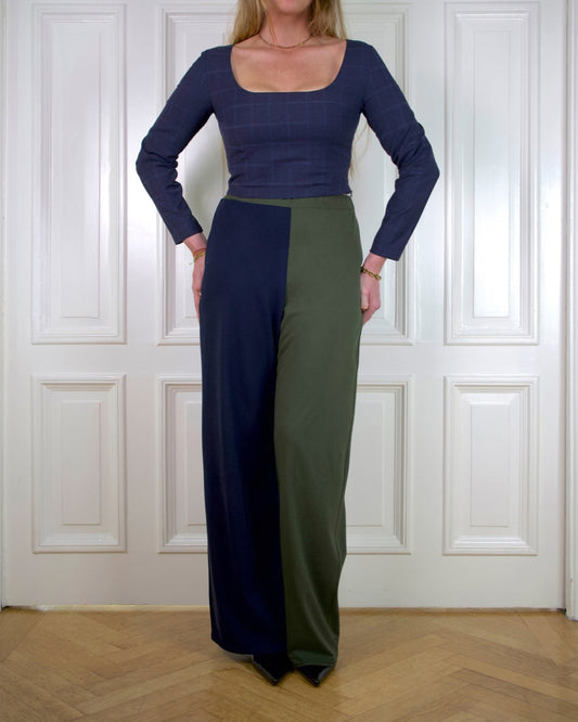 Woman standing in front of a panel wall wearing a navy blue long sleeve top with a pair of wide pants in moss green and navy blue