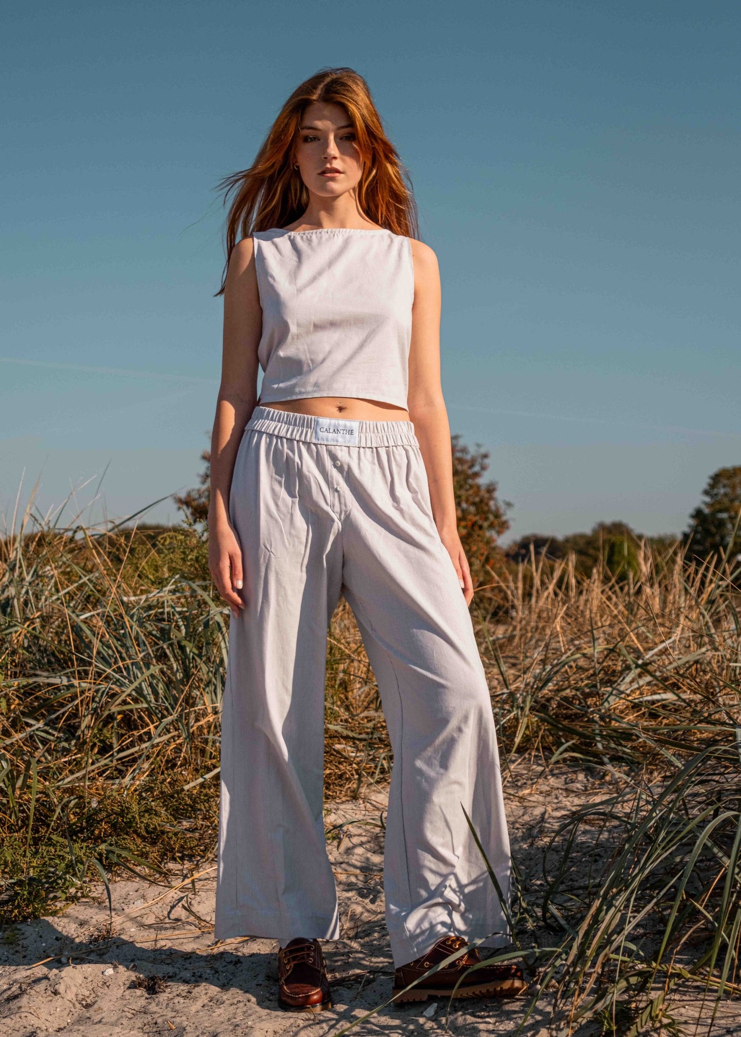 Model_standing_on_the_beige_in_a_full_calanthe_set_of_beige_top_and_beige_boxer_pants_with_white_calanthe-logo