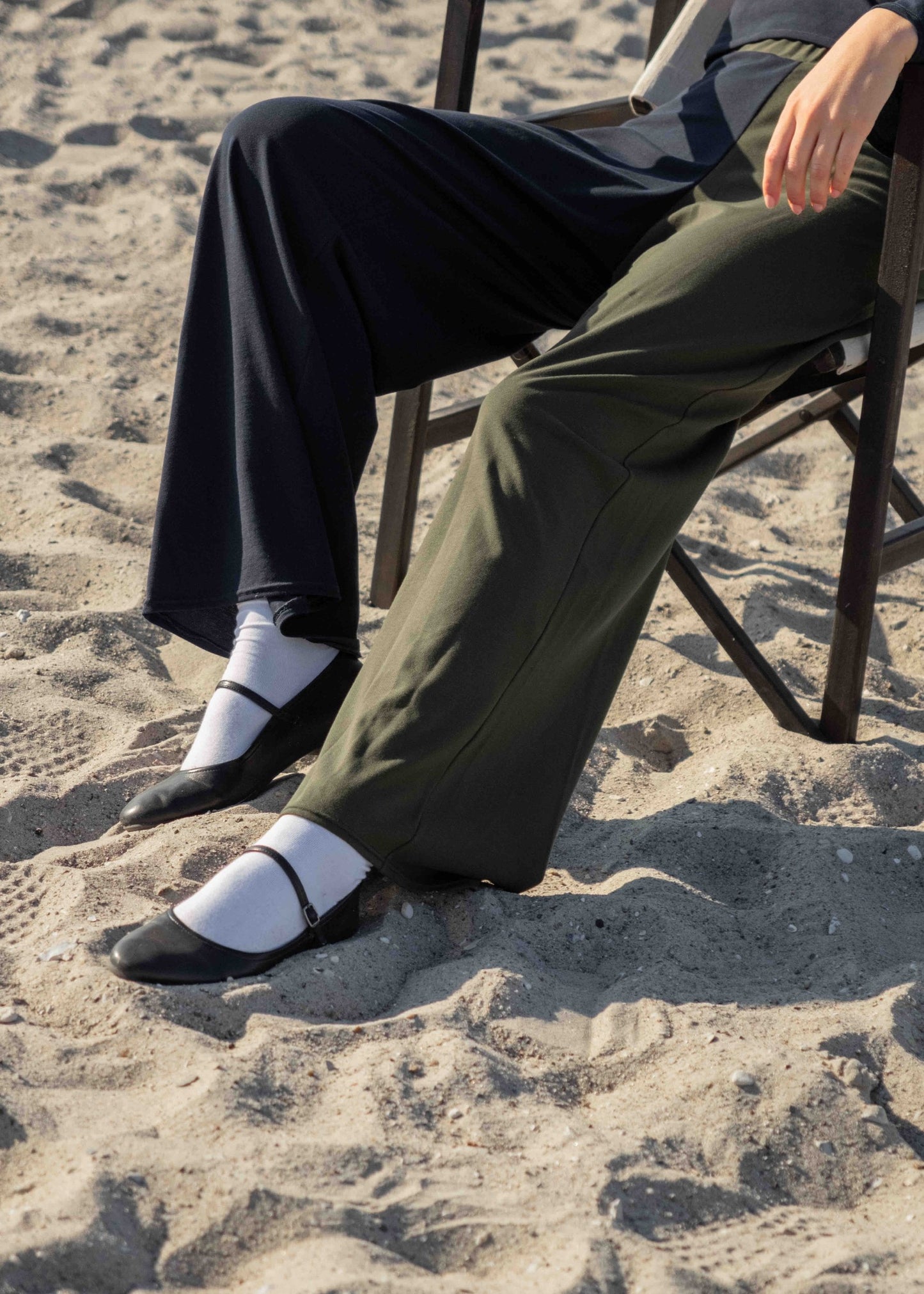 Model_sitting_in_chair_at_the_beach_wearing_the_matilda_pants_from_calanthe_with_one_navy_blue_leg_and_one_moss_green_with_white_socks_and_mary_janes