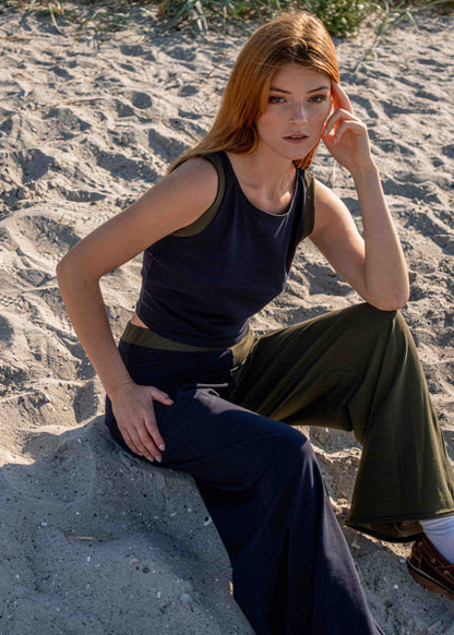 Model_sitting_down_in_beach_sand_in_Calanthe_set_of_Matilda_pants_and_jenny_top_both_in_navy_blue_and_moss_green_cotton_fabric_with_color_block_details